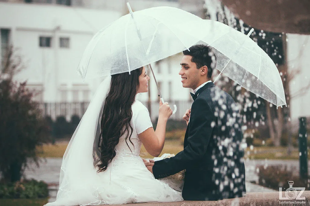 Novios conversando bajo un paraguas transparente en un matrimonio con lluvia en Concepción