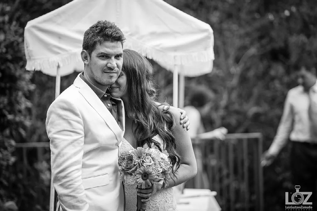 Novio de terno blanco abrazando a la novia durante la recepción en el jardín
