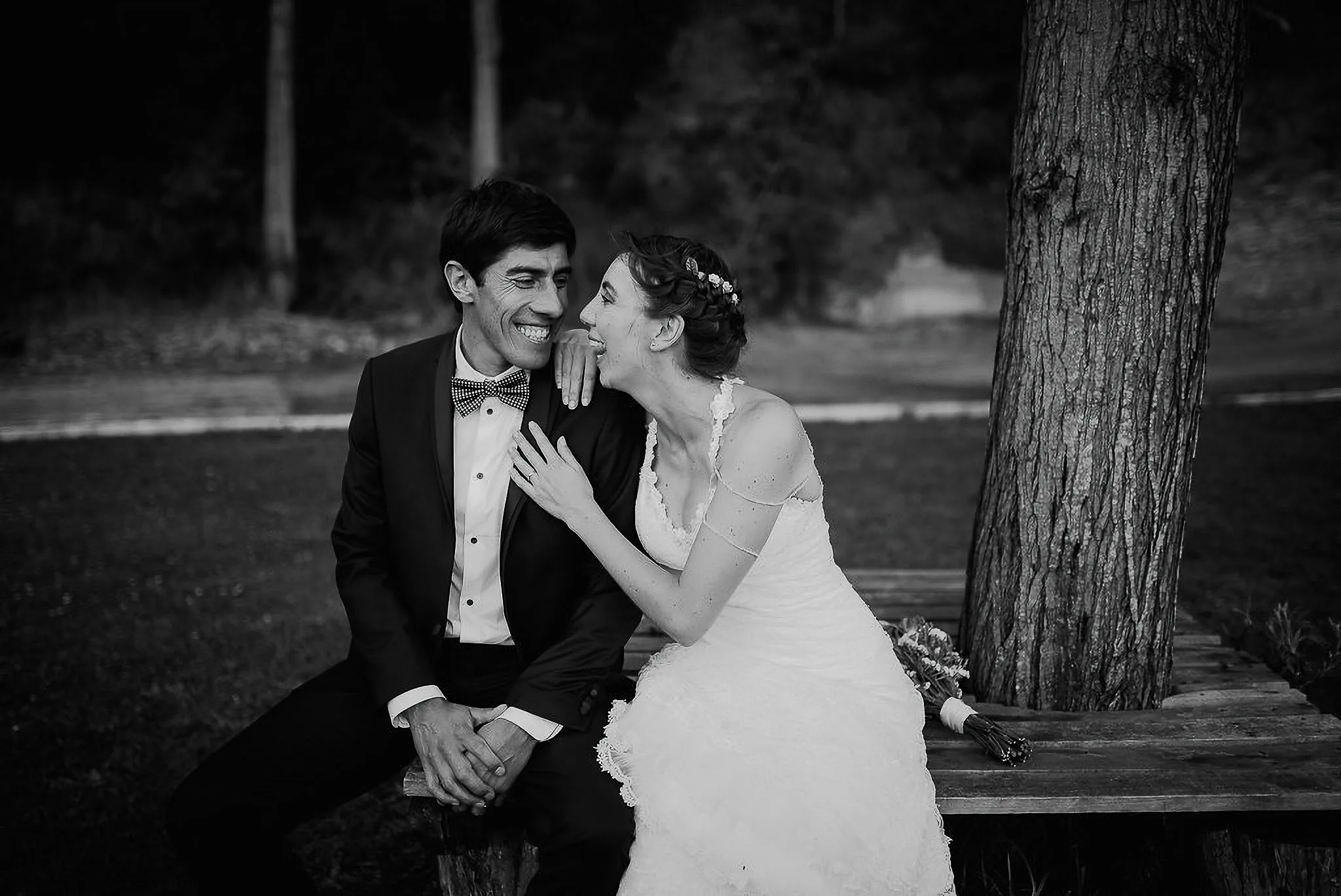 Novia riendo junto al novio sentados bajo un árbol, blanco y negro