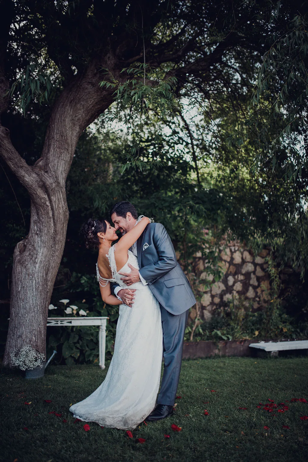 Beso de los novios bajo un árbol en el jardín del centro de eventos
