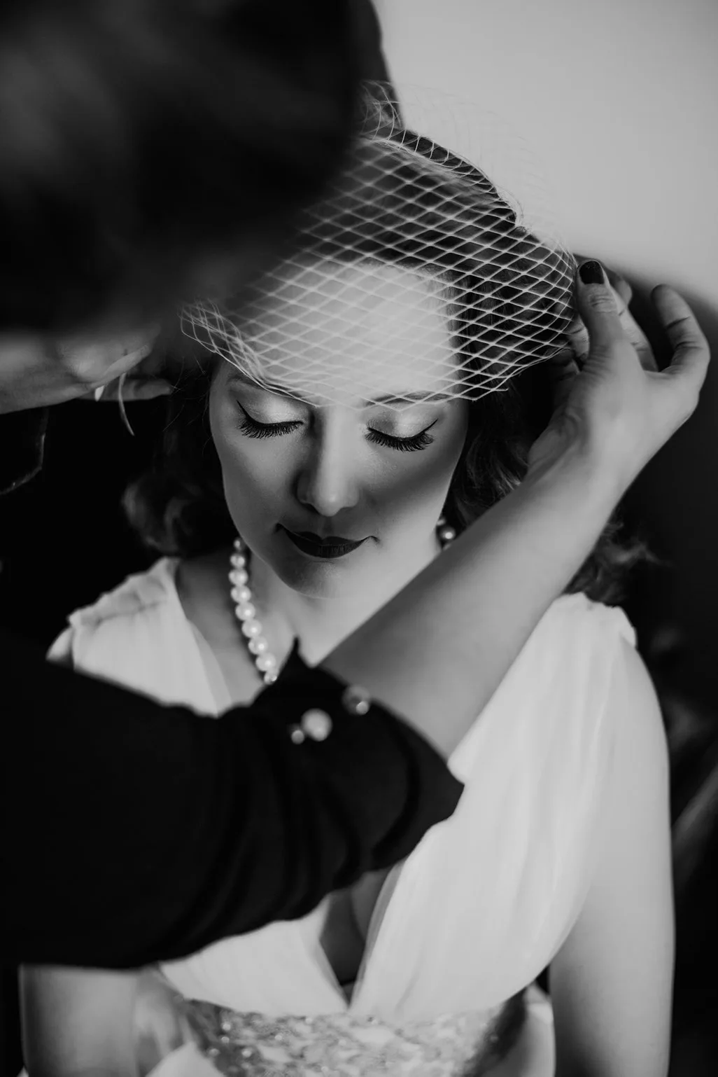 Novia con tocado de rejilla ajustándose el peinado, retrato en blanco y negro