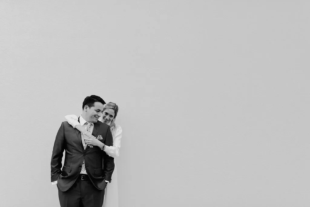 Novios abrazados contra un muro blanco, retrato minimalista en blanco y negro