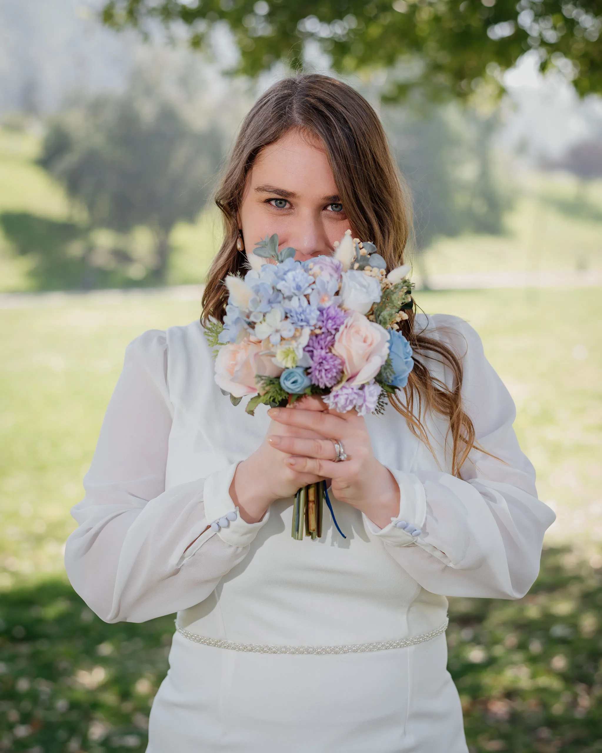 Novia asomando la mirada tras su ramo de flores en tonos pastel